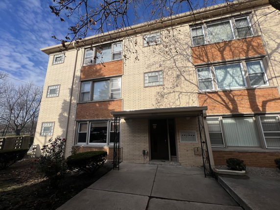 Front view of a multi-story residential building with large windows and a small entrance porch.