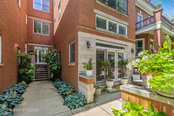 Front view of a brick multi-story house with large windows and a small patio area.