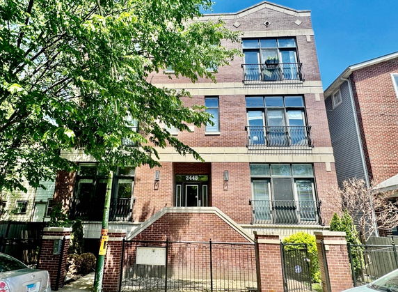 Front view of a multi-story brick building with balconies and stairs leading to the entrance.