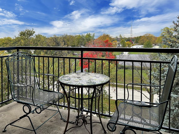 Balcony with metal chairs and table overlooking a scenic view of trees and a distant tower.