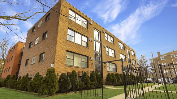 Front view of a multi-story brick residential building with multiple windows and a gated entrance.