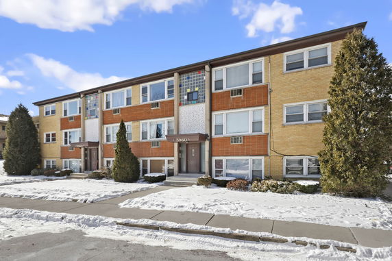 Front view of a three-story apartment building with brick exterior and snow-covered surroundings.