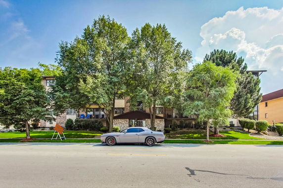 Front view of a multi-story residential building with a trees and a car parked in front.