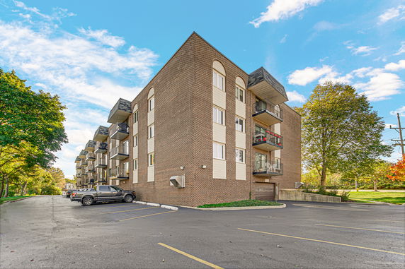 Front view of a multi-story brick apartment building with balconies and parking area.