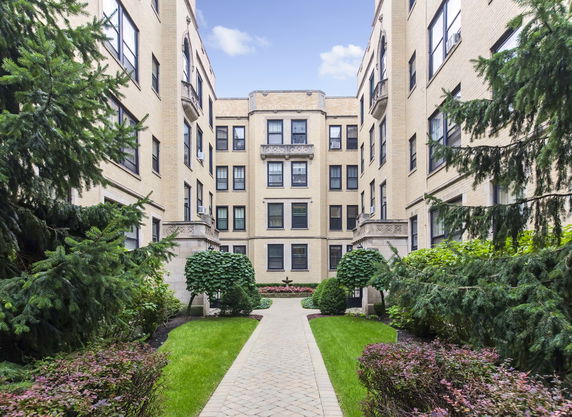 Front view of a multi-story brick apartment building with manicured garden path.