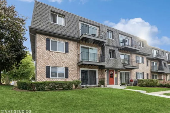 Front view of a multi-story residential building with balconies and red entrance door.