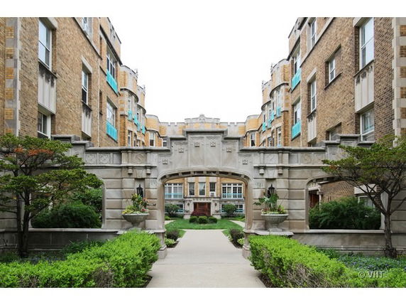 Front view of a multi-story brick building with decorative archway and landscaping.