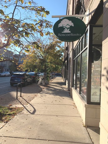 Sidewalk view in front of a building with a bookstore sign and trees lining the street.