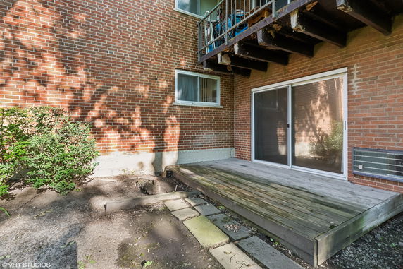 Rear view of a brick building with a small wooden deck and sliding glass door.