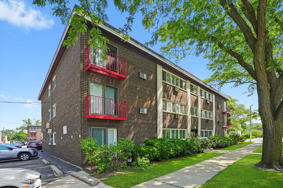 Front view of a three-story brick apartment building with red balconies.
