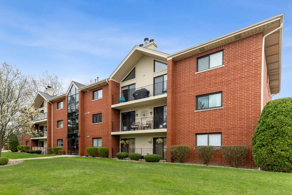 Front view of a multi-story red brick apartment building with balconies.