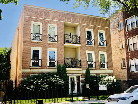 Front view of a three-story brick apartment building with balconies.