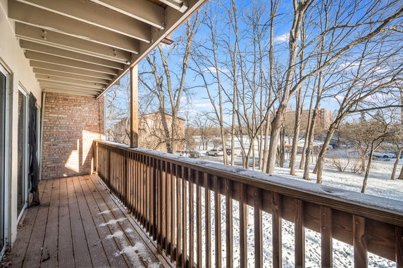View from a wooden balcony looking out over a snowy landscape with trees and buildings.