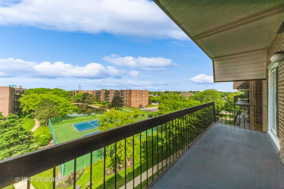 Wide-angle view from a balcony overlooking tennis courts and apartment buildings.