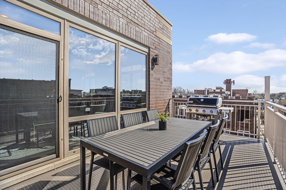 Rooftop area with dining table, chairs, and a barbecue grill.