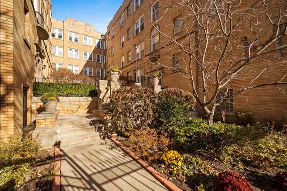 Front view of a multi-story brick apartment building with decorative plants and stairs.
