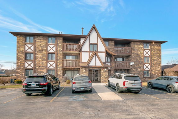 Front view of a multi-story apartment building with balconies and parking in front.