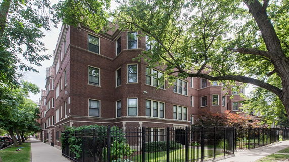 Front view of a multi-story brick building with numerous windows and a gated perimeter.