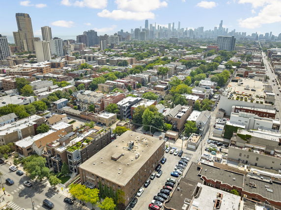 Aerial view of an urban area with multiple residential and commercial buildings, greenery, and distant city skyline.
