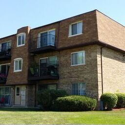 Front view of a three-story brick apartment building with balconies.