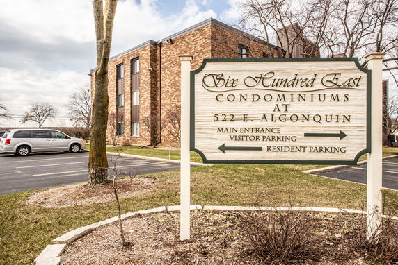 Front view of a brick condominium building with a sign and parking area.
