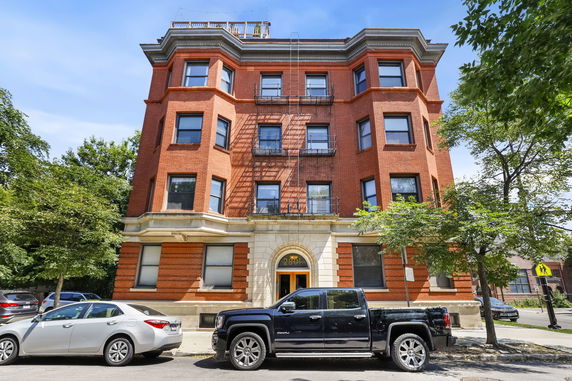 Front view of a multi-story red brick building with a central entrance and fire escapes.