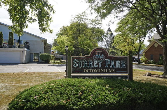 Front view of a condominium building with a parking area and a sign reading 'Surrey Park Condominiums'.