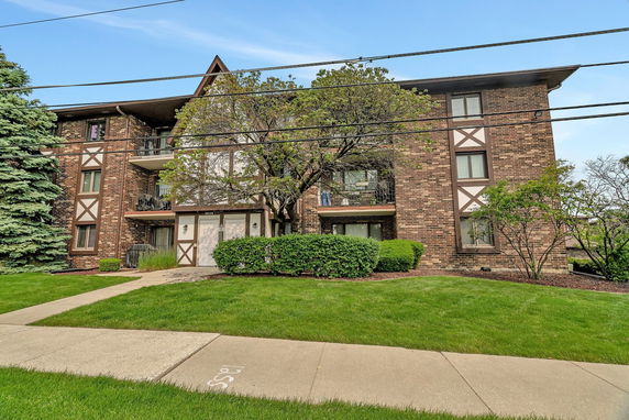 Front view of a multi-story brick apartment building with a gabled roof and balconies.
