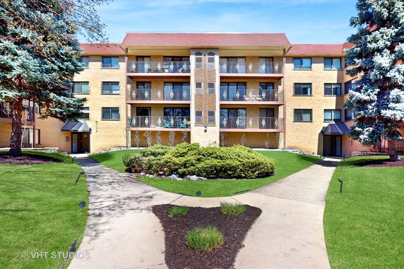 Front view of a multi-story apartment building with balconies and a sloped roof.