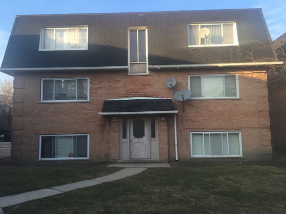 Front view of a three-story brick building with dormer windows and a pitched roof.