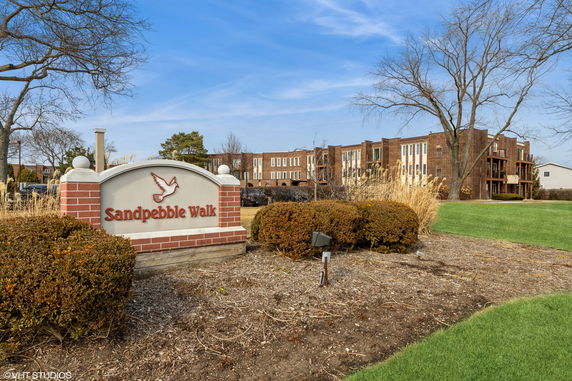 Front view of a multi-story brick residential building with a 'Sandpebble Walk' sign.