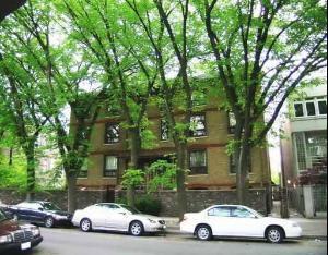 Front view of a multi-story building with trees and parked cars in front.