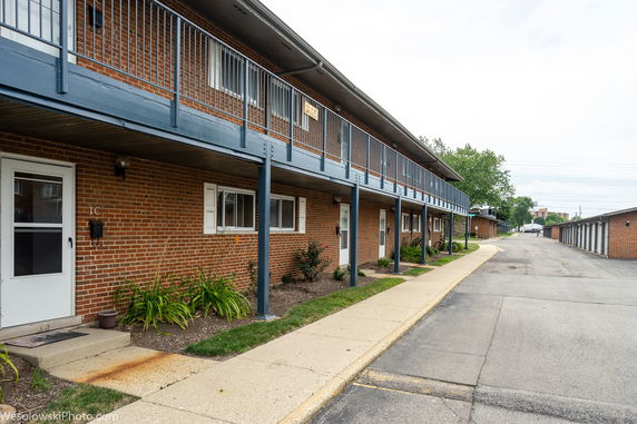 Front view of a two-story brick apartment building with a walkway on the upper level.