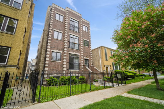 Front view of a multi-story brick building with a gated entrance.
