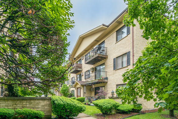 Front view of a multi-story brick building with balconies and shrubs.