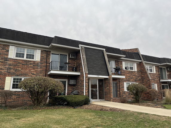 Front view of a two-story brick building with balconies and a pitched roof.