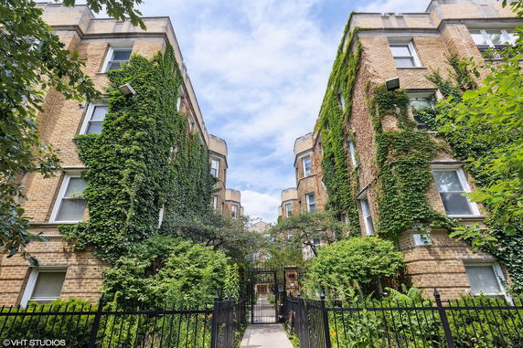 Front view of a brick apartment building with ivy-covered walls and a gated entrance.
