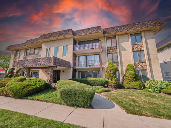 Front view of a multi-story apartment building with balconies and a textured roof.