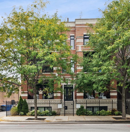 Front view of a multi-story brick building obscured by trees.