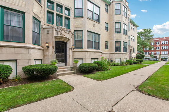 Front view of a multi-story apartment building with architectural details and green window frames.