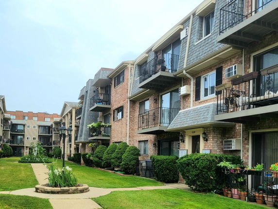 Front view of a multi-story brick apartment building with balconies and a landscaped pathway.