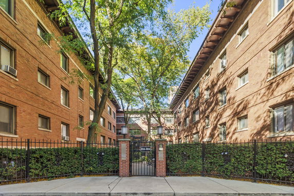 Front view of a multi-story brick apartment building with a gated entrance.