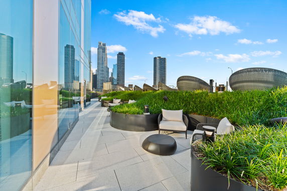 Rooftop terrace with seating and greenery, surrounded by tall city buildings.