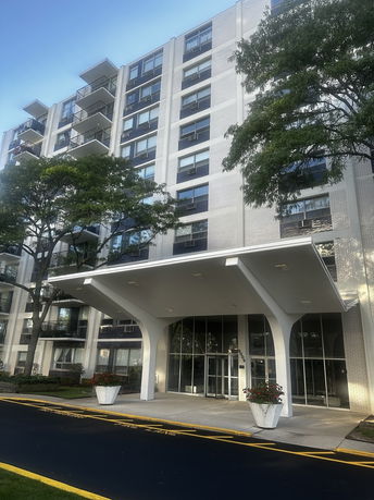 Front view of a multi-story apartment building with balconies and a covered entrance.