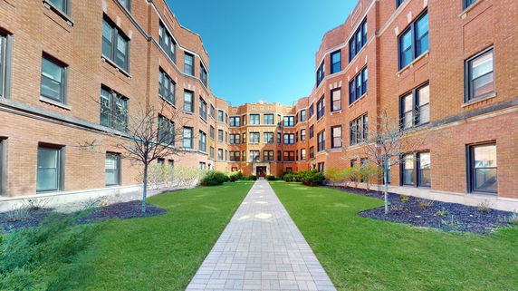 Front view of a multi-story brick apartment building with a central courtyard.