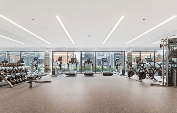 Interior view of a modern gym room with exercise equipment including treadmills and stationary bikes.