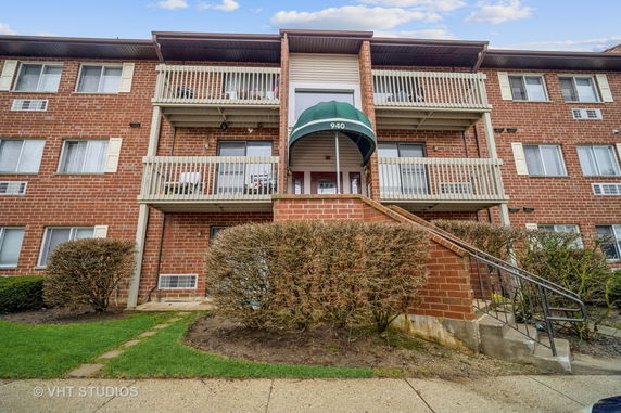 Front view of a three-story brick apartment building with balconies.