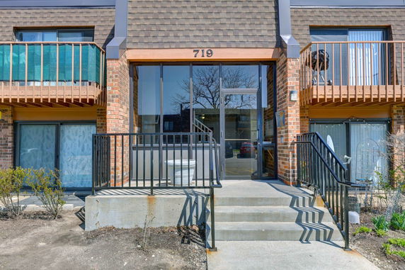 Front view of a brick apartment building with balconies and glass entrance door.