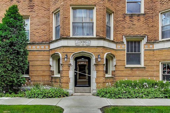 Front view of a brick building entrance with archway and symmetrical windows.