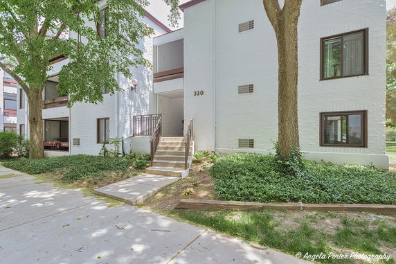 Front view of a multi-story residential building with white exterior walls and a small staircase leading to the entrance.